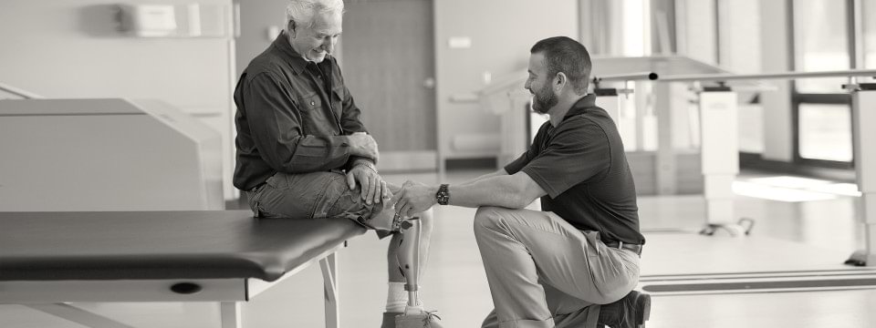 A therapist kneeling as he helps a patient wearing an Ottobock Kenevo prosthesis