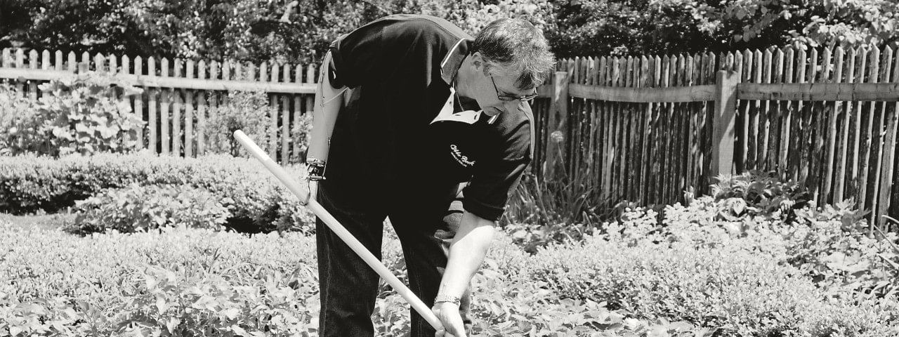 Man raking a garden while wearing body-powered hook